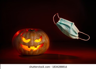 
Illuminated halloween pumpkin with devilish face and coronavirus protective surgical mask flying on one side. New normal - Powered by Shutterstock