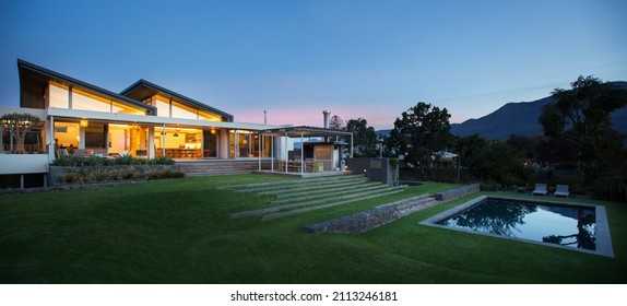 Illuminated modern house beyond yard and swimming pool at night
