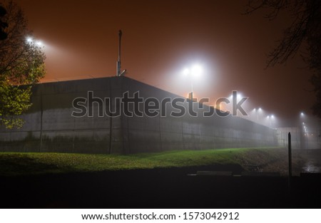 Illuminated, modern prison wall on a foggy evening.