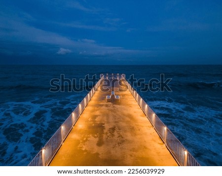 illuminated pier with dramatic sky over stormy dark sea at evening aerial view, Varna Bulgaria