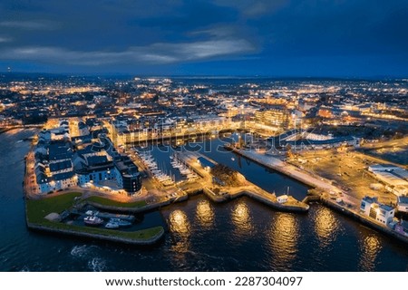 Illuminated port town at night. Aerial view on River Corrib and Galway city, Ireland. Dark sky. Popular educational center and tourist hub with vivid night life.