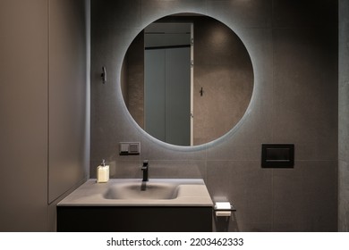 Illuminated round mirror in a dark bathroom interior - Shutterstock ID 2203462333