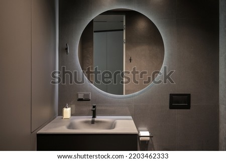 Illuminated round mirror in a dark bathroom interior