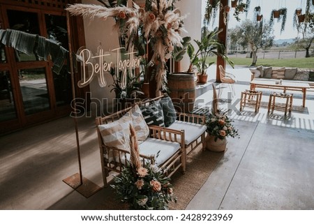 Illuminated sign that says better together. Decorative corner for an outdoor party, consisting of a two-seater sofa, floral ornaments and a neon sign.