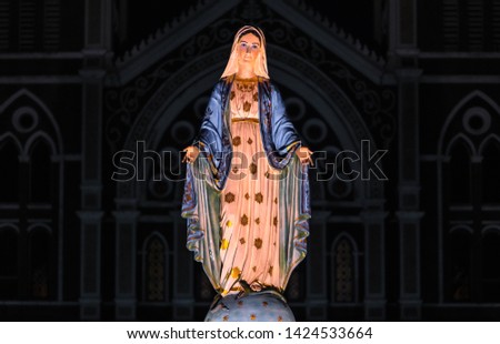 illuminated statue of mother Mary of roman catholic with front view of christian church in dark background