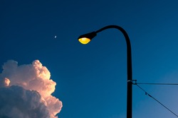 Illuminated Street Light And Pole Against Blue Evening Sky With Cloud And Moon.

