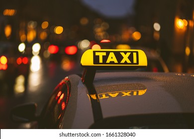 Illuminated taxi sign on top of a car. City lights with neon color in the background. Rainy urban night scene.