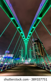 Illuminated vibrant steel cable-stayed suspension bridge at The Lowry in Salford Quays, Greater Manchester, UK.