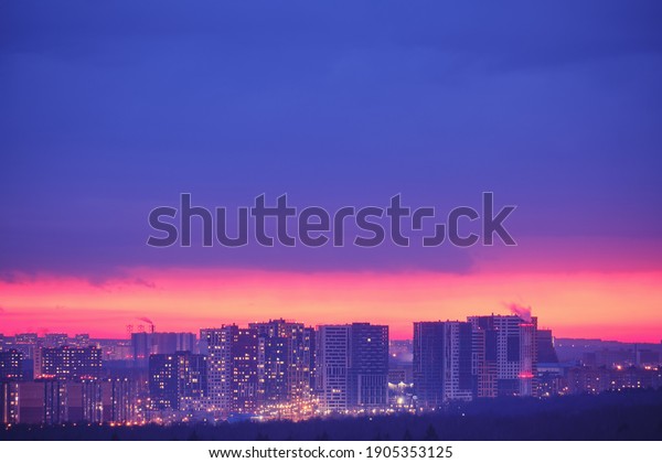 Illuminated windows of the night city house and\
roads with cars. Pink evening sunset over modern Moscow, Russia.\
Top view of the city at\
dusk