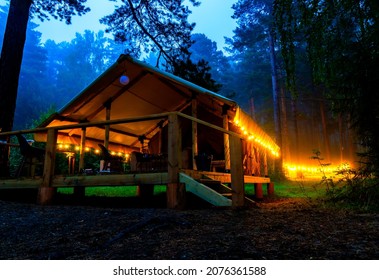 Illuminated yellow camping bell tent at night. Glamping bell tent glows at forest.