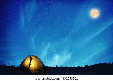 Illuminated Yellow Camping Tent Under Many Stars And Full Moon At Night