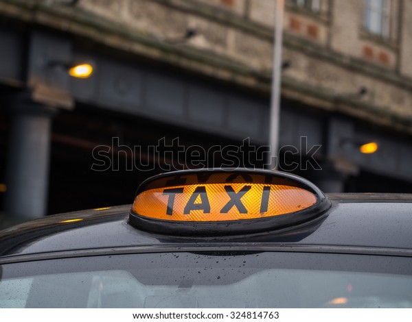 Illuminated yellow taxi sign on\
a typical old style black taxi in Manchester, Great Britain. Close\
up.