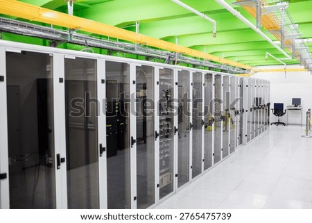 Illustrating flat datacenter switch racks under yellow trays and beams, raised tiles, desk monitors. Technology, infrastructure, data, networking, automation, modern, industrial