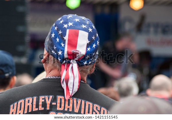 Illzach - France -9 June 2019 - Portrait\
of Harley Dadson biker with american flag on haed on back view at\
rock n roll concert at fun car show\
event