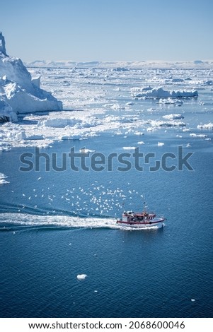 Ilulissat, Greenland - May 23: A fishing vessel returning to Ilulissat with lots of seagulls in its tail through the ice fjord