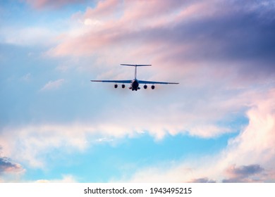 Ilyushin Aircraft Seen From Behind During Take Off At Low Altitude With Sunset Colors Shades. Russian Four-engine Airplane Silhouette Surrounded By Pink Clouds And Blue Sky. Russian Plane Constructor.