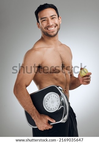 Im doing everything I can to maintain a healthy weight. Shot of an athletic young man holding an apple and a weighing scale.