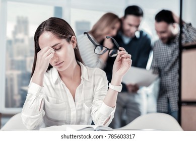 Im Exhausted. Tired Serious Pretty Woman Sitting In The Room By The Table And Holding The Glasses And Feeling Bad Herself.