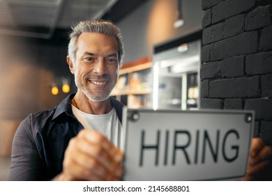 Im Looking For Some New Staff Members. Cropped Portrait Of A Handsome Mature Man Holding Up A Hiring Sign While Standing In His Coffee Shop.