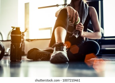 Sportvrouw die zit en rust na het sporten of sporten in de fitnessruimte met eiwitshake of drinkwater op de vloer. Ontspan concept. Krachttraining en Body build-up thema. Warme en koele toon