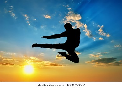 siluet seorang pria yang terbang dengan latar belakang langit matahari terbenam. Komposisi seni bela diri.