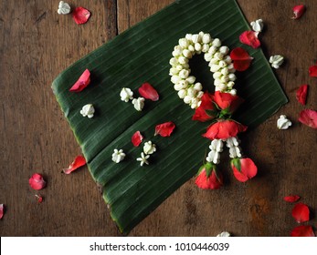 Thaise slinger van roos, jasmijn en witte kroonbloem op bananenblad met rozenblaadjes op hout.