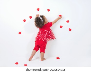 Une petite fille métisse décore un mur blanc avec des coeurs rouges pour la Saint-Valentin