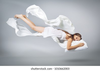 Sleeping girl. Flying in a dream. White linen flying through the air. Light grey background