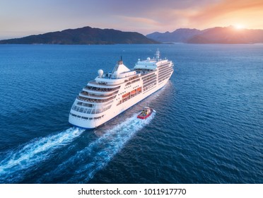 Cruise ship at harbor. Aerial view of beautiful large white ship at sunset. Colorful landscape with boats in marina bay, sea, colorful sky. Top view from drone of yacht. Luxury cruise. Floating liner