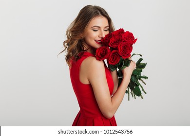 Portrait of an attractive young woman dressed in red dress holding bouquet of roses isolated over white background