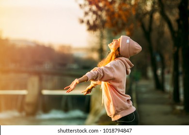 cool hipster young girl in pink hoodie standing by a river in the city very happy smiling to the sun and enjoying it, on autum or springtime