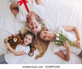 Top view of little girl, her attractive young mother and charming grandmother are lying on bed while spending time together at home. Women's generation. International Women's Day. Happy Mother's Day.