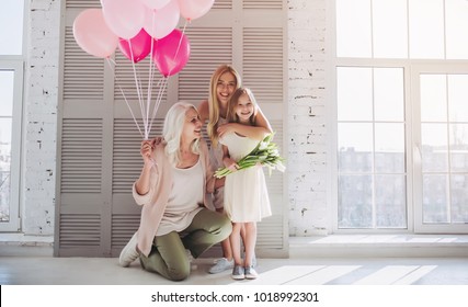 Kleines süßes Mädchen, ihre attraktive junge Mutter und charmante Großmutter stehen mit Luftballons und Blumen im hellen Raum. Frauengeneration. Internationaler Frauentag. Schönen Muttertag.