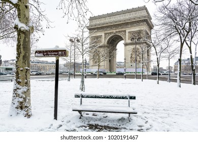 Winter in Paris im Schnee. Der Arc de Triomphe mit einer schneebedeckten öffentlichen Bank im Vordergrund.