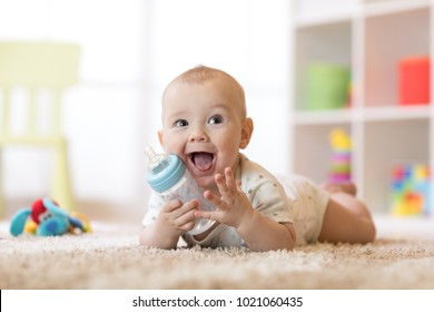 Bé trai dễ thương bú bình. Đứa trẻ nằm trên thảm trong nhà trẻ ở nhà. Smiling con được 7 tháng tuổi.