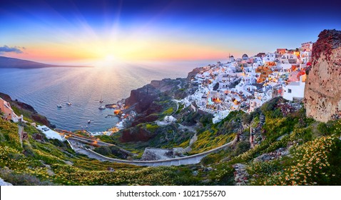 Fira Stadt auf Santorini Insel, Griechenland. Unglaublich romantischer Sonnenuntergang. Oia Dorf im Morgenlicht. Erstaunliche Sonnenuntergangsansicht mit weißen Häusern. Inselliebhaber. Panorama der Bucht. Santorini Blumen.