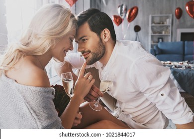 True love. Beautiful young couple drinking champagne and smiling while sitting face to face in the bedroom