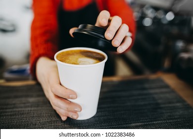 Barista in Schürze hält heißen Cappuccino in weißen Pappbechern zum Mitnehmen in den Händen. Kaffee zum Mitnehmen im Café-Shop