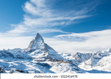 Scenic view on snowy Matterhorn peak in sunny day with blue sky and dramatic clouds in background, Switzerland.