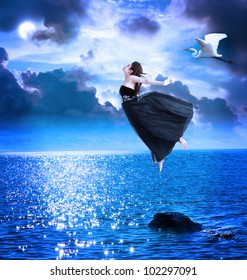 Beautiful girl jumping into the blue night sky with white egret