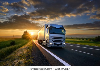Vrachtwagen rijden op de asfaltweg in landelijk landschap bij zonsondergang met donkere wolken