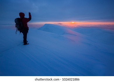 Mann auf einem Berggipfel während eines atemberaubenden Sonnenaufgangs, über den Wolken, mit triumphierender Geste – Freiheit in den winterlichen Bergen der Niederen Tatra, Slowakei.