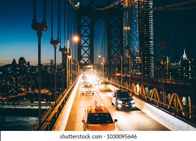 Metropolitan traffic on Brooklyn bridge with vehicles shining with evening light, yellow cab taxis driving from Manhattan to another district, River crossings, Environmental impact reduction concept