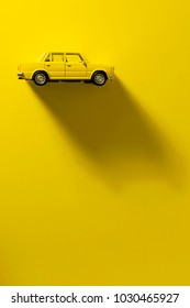 Gele speelgoedauto op een gele achtergrond met lange en zijschaduw.