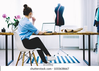 Góc nhìn Bacl của nữ doanh nhân duyên dáng đang ngồi trước máy tính để bàn với các thiết bị may mặc và phân tích thông tin từ máy tính xách tay với màn hình trống cho quảng cáo thời trang của bạn được kết nối với wifi