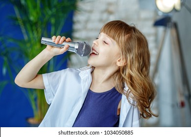 Little beautiful child singing into the microphone. The concept is childhood, lifestyle, music, singing, listening, hobbies.