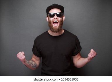 グレイの背景にロゴやデザイン用のスペースを持つ黒い空のTシャツを着たひげを持つ流行に敏感なハンサムな男性モデル