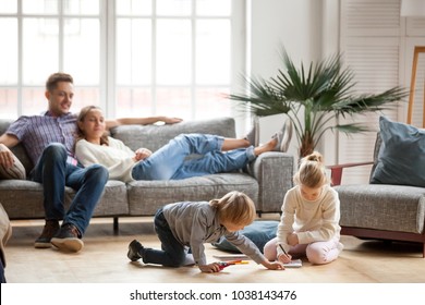 Kinder Schwester und Bruder spielen zusammen zeichnen auf dem Boden, während junge Eltern zu Hause auf dem Sofa entspannen, kleines Jungenmädchen, das Spaß, Freundschaft zwischen Geschwistern, Familienfreizeit im Wohnzimmer hat