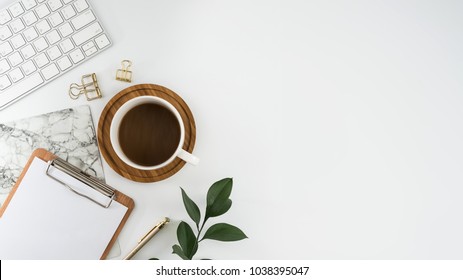 Flat lay, top view office table desk. Workspace with blank clip board, keyboard, office supplies, pencil, green leaf, and coffee cup on white background.