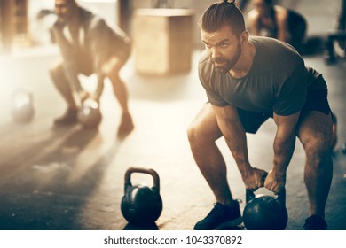 Fit jonge man in sportkleding gericht op het optillen van een halter tijdens een oefenles in een sportschool
